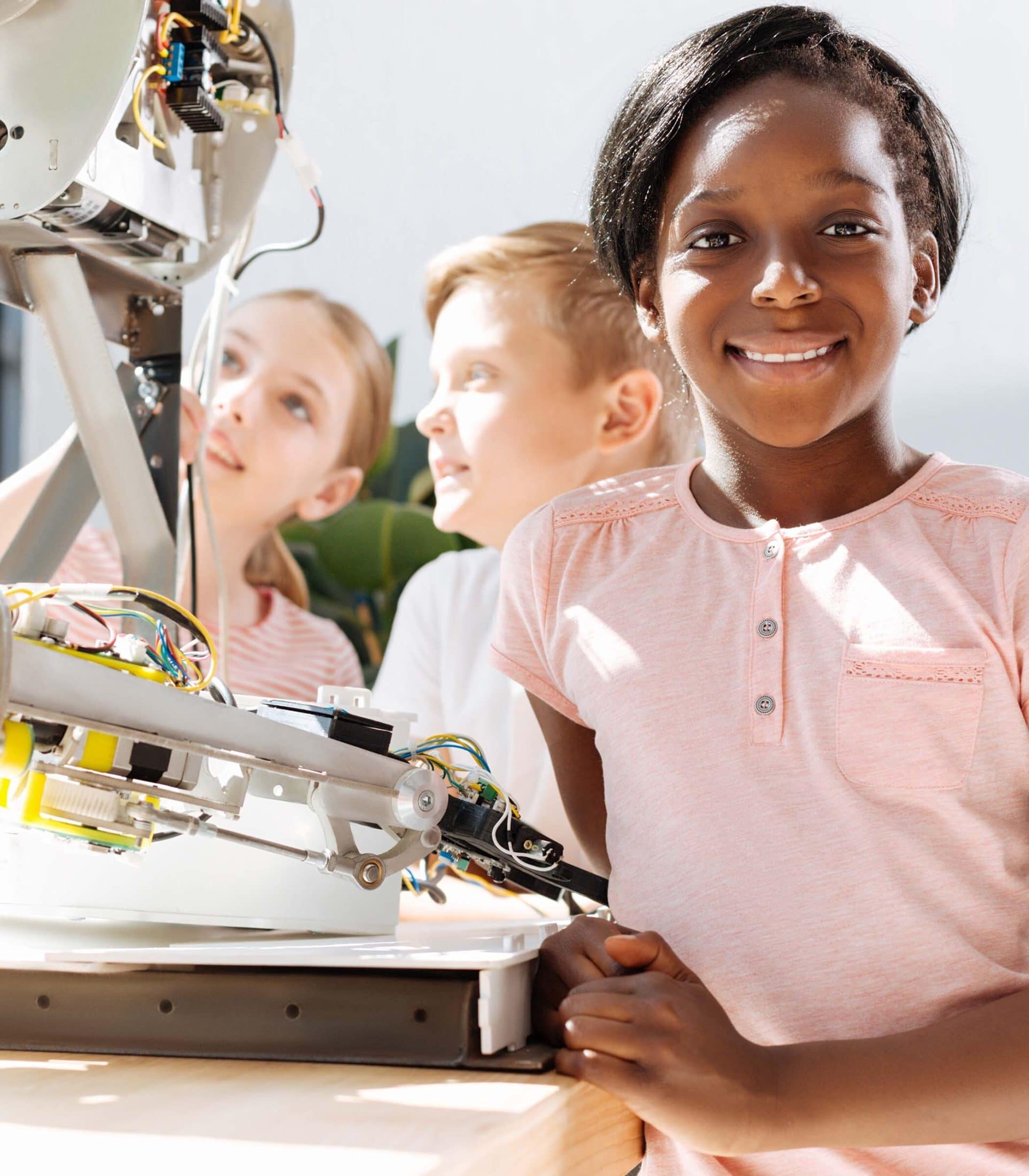 young smiling black girl in a pink shirt working in a robotics lab
