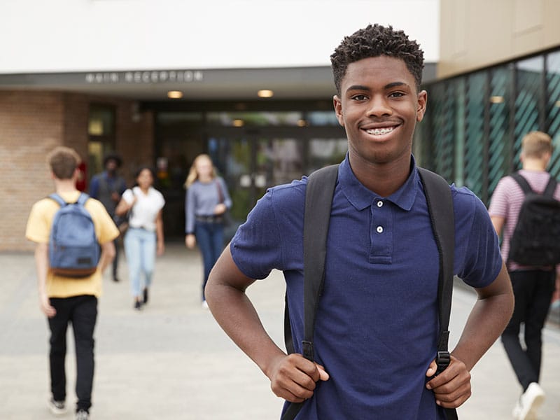 smiling student standing in front of school